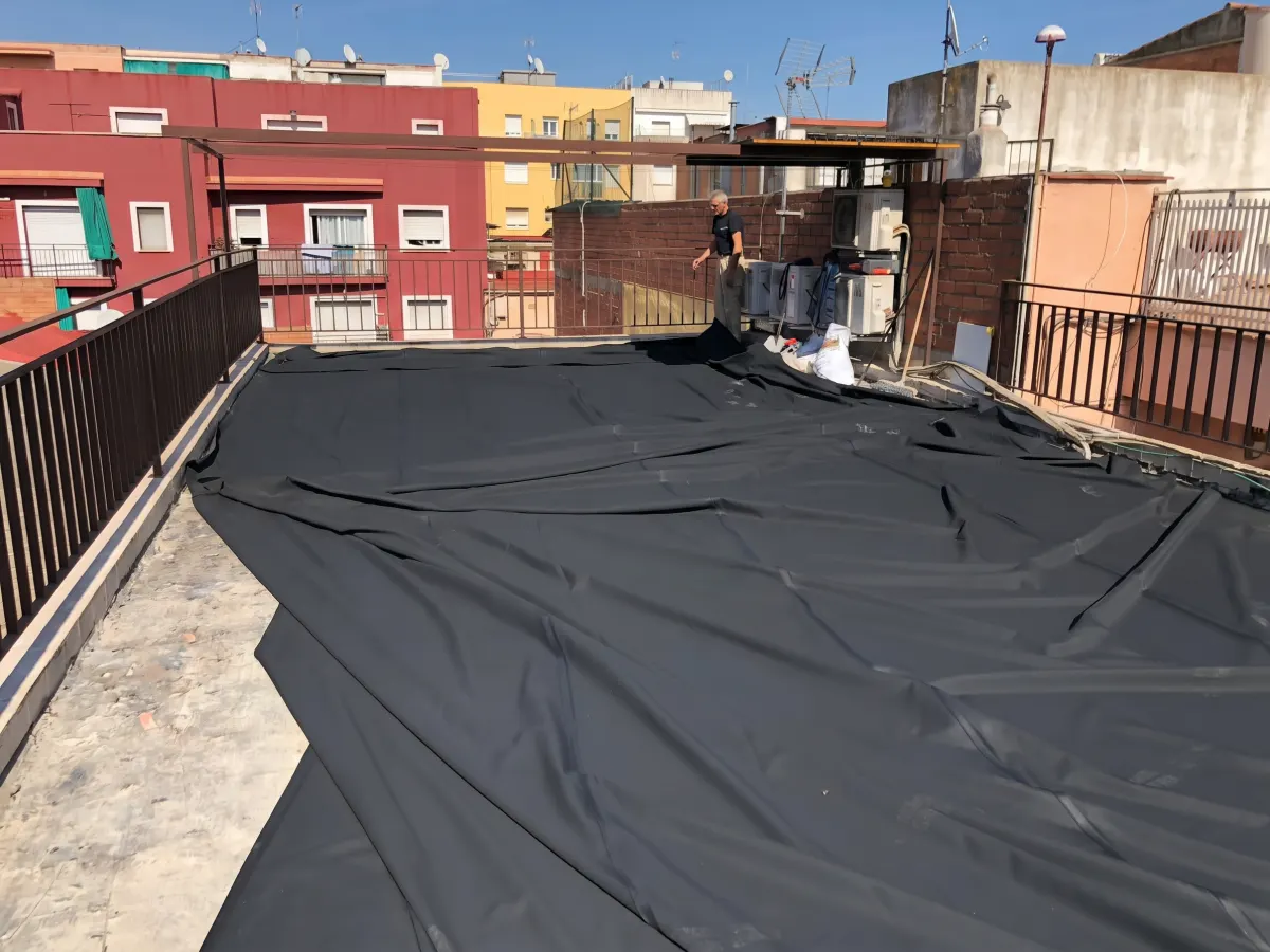 Operari de Pamolux col·locant una làmina impermeable negra sobre tota la superfície d'un terrat